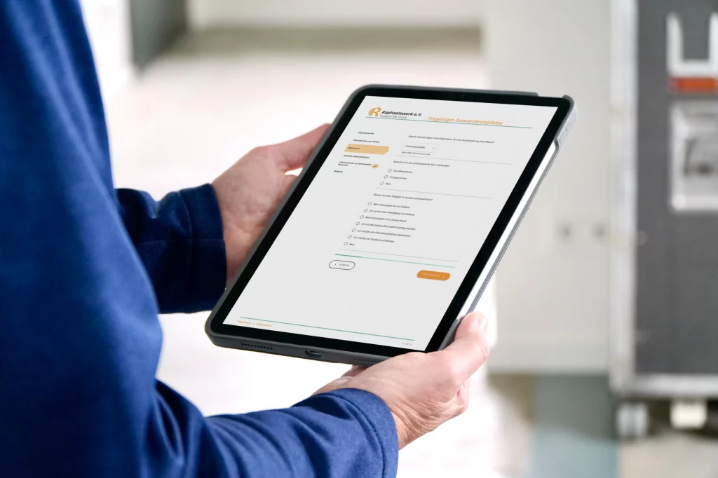 Person h&auml;lt ein Tablet, auf dem der digitale Auswanderungslotse angezeigt wird.