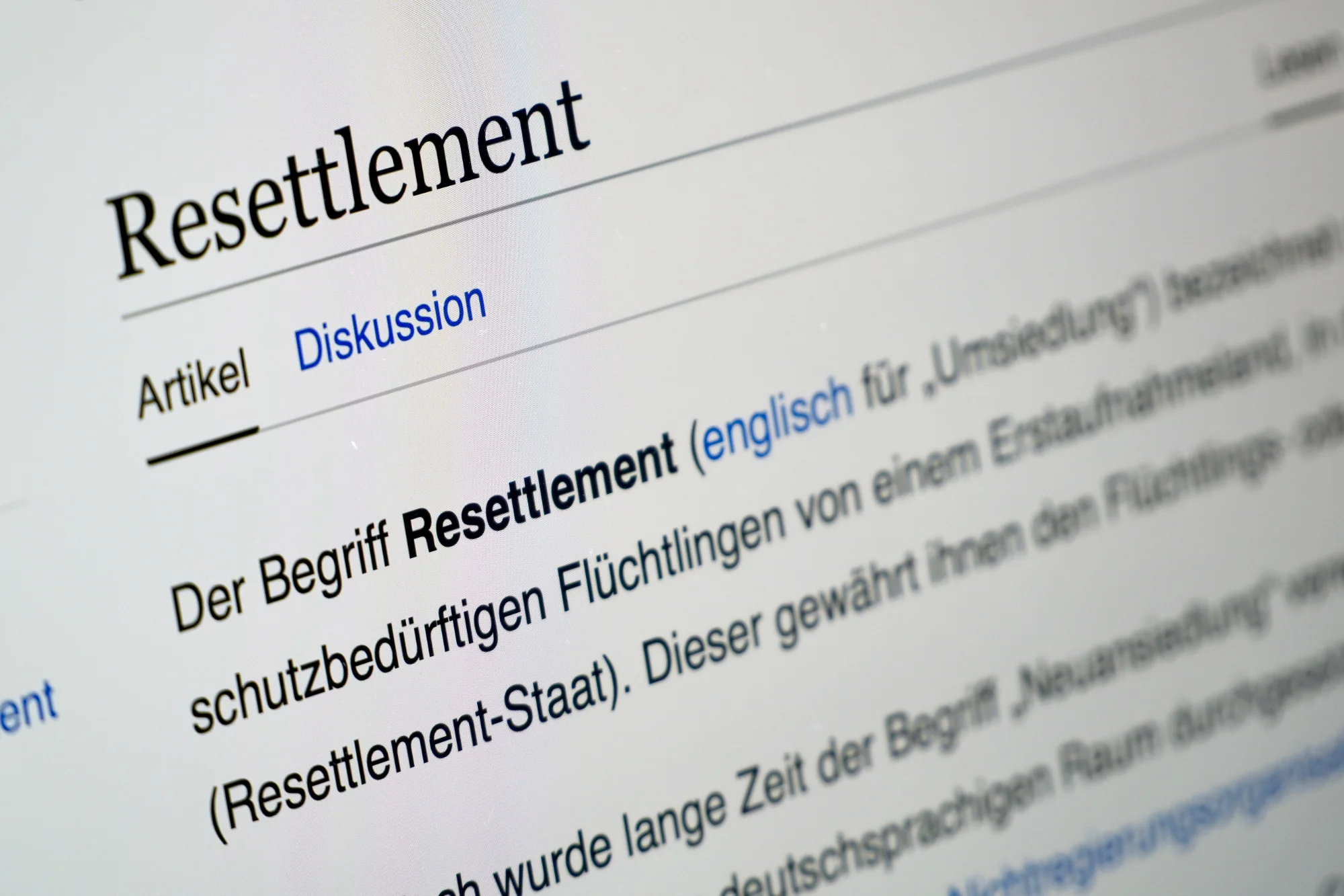 Nahaufnahme eines Computerbildschirms, der die deutsche Wikipedia-Seite zum Thema Resettlement anzeigt, wobei die Abschnitte für Artikel und Diskussion sichtbar sind.